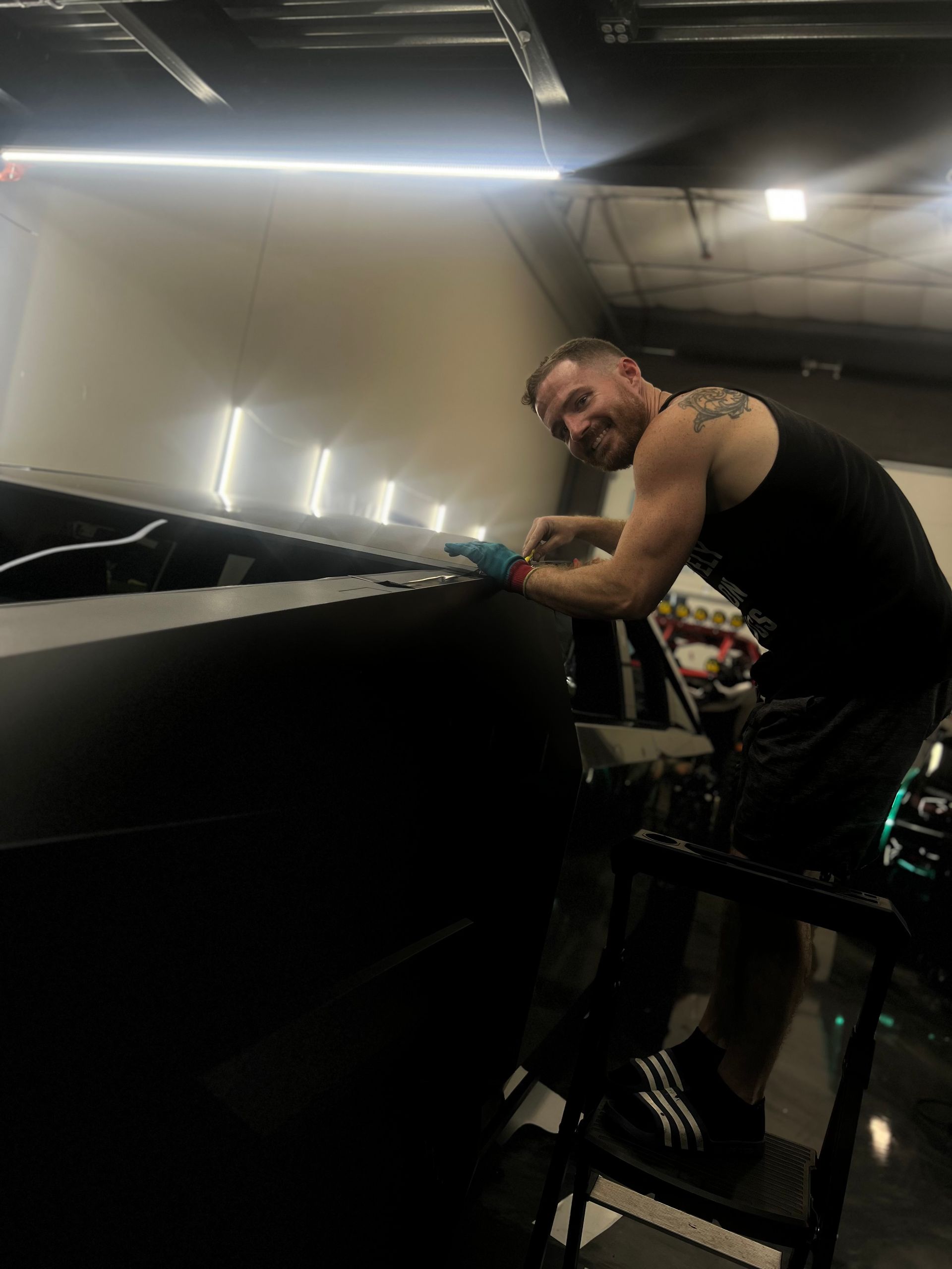 A man is kneeling on a stool in front of a machine.