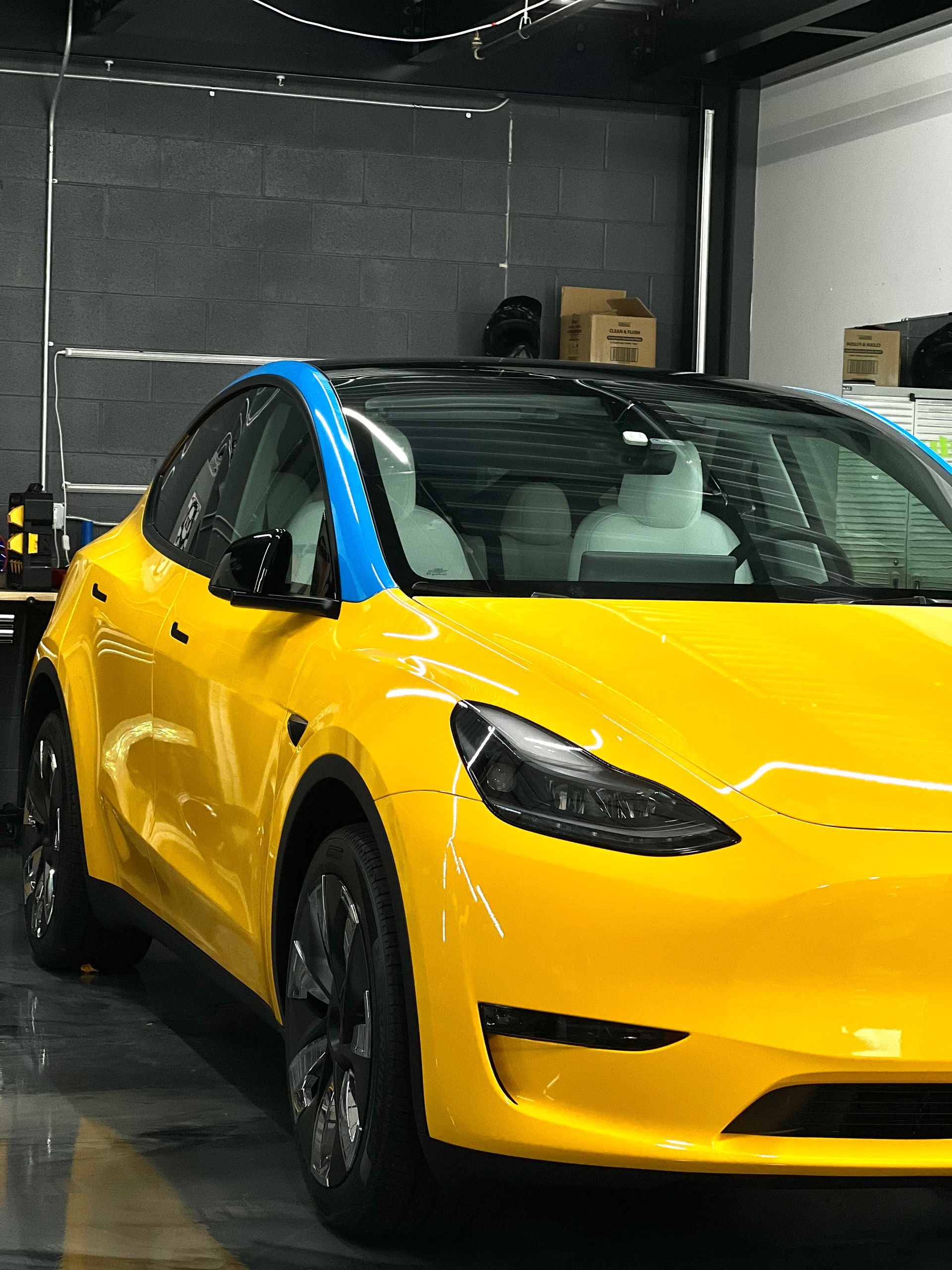 A yellow tesla model y is parked in a garage.
