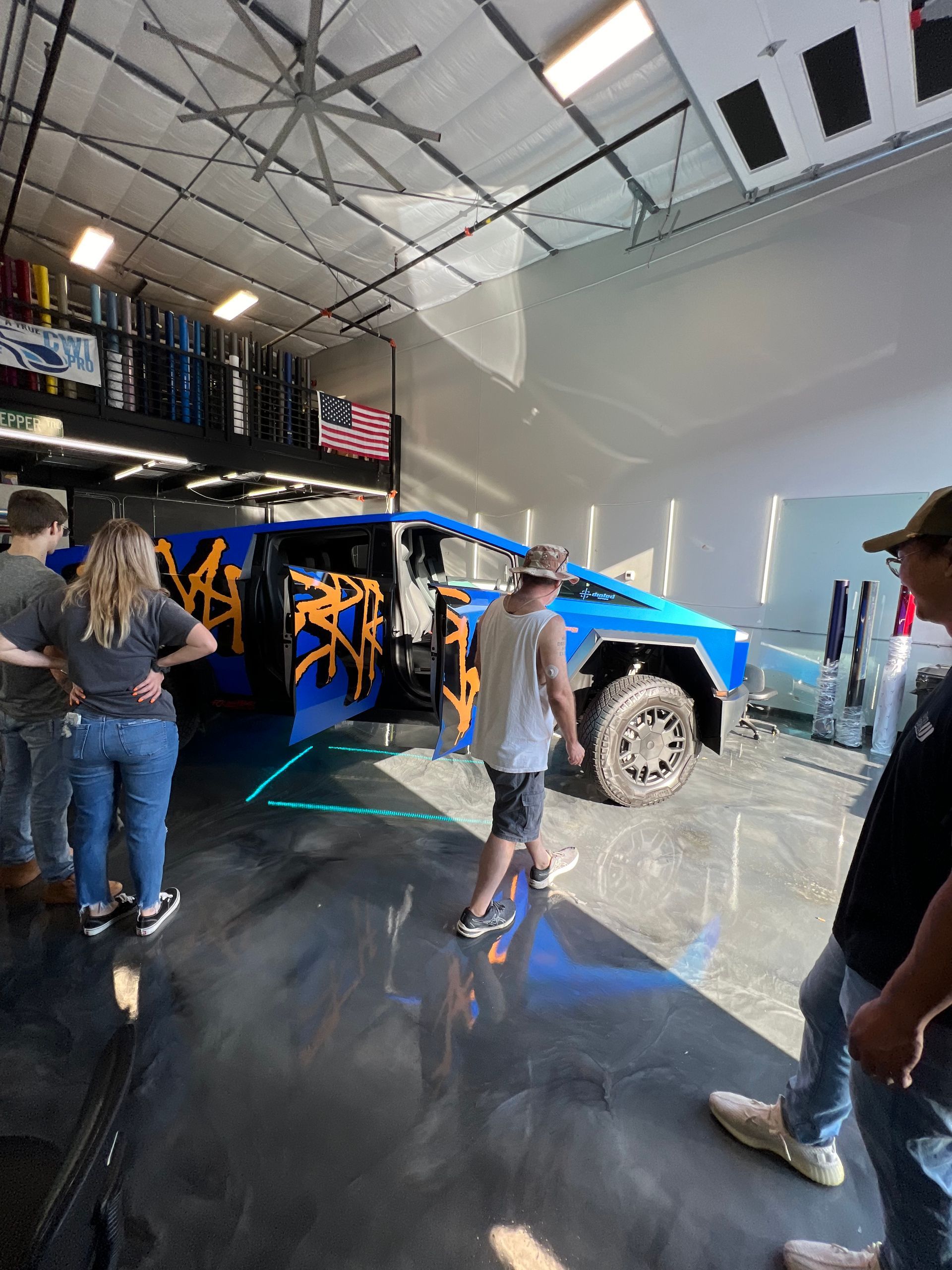 A group of people are standing around a blue truck in a garage.