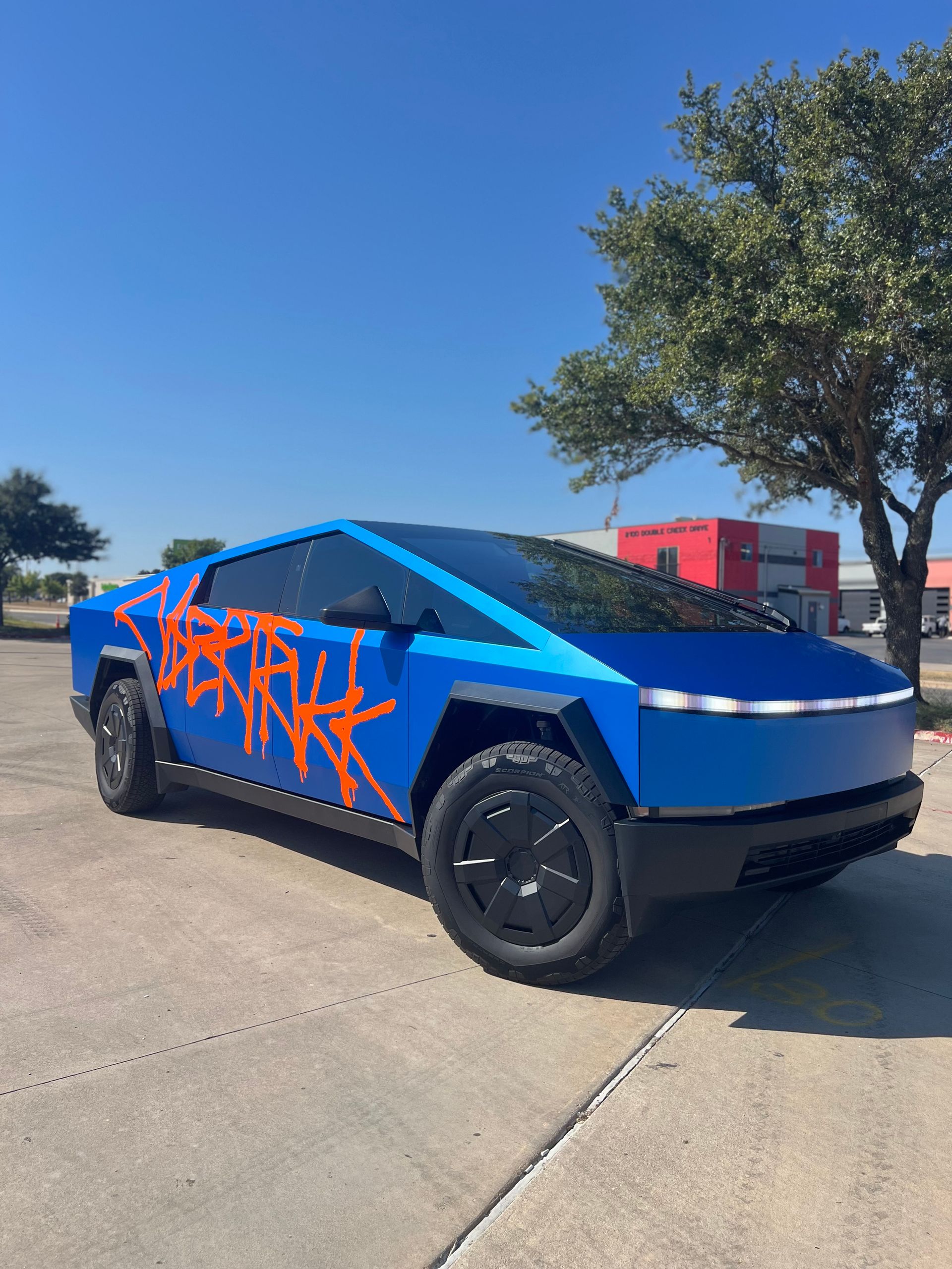 A blue and orange tesla cybertruck is parked on the side of the road.