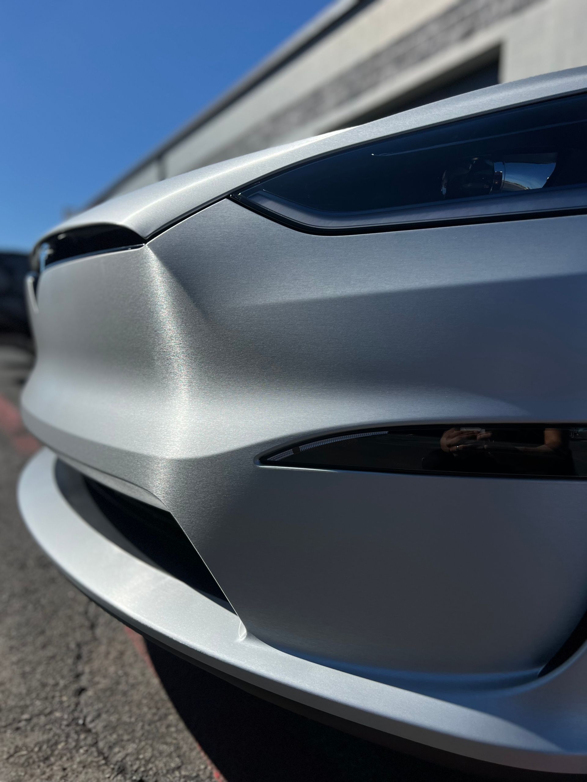 A silver tesla model 3 is parked in front of a building