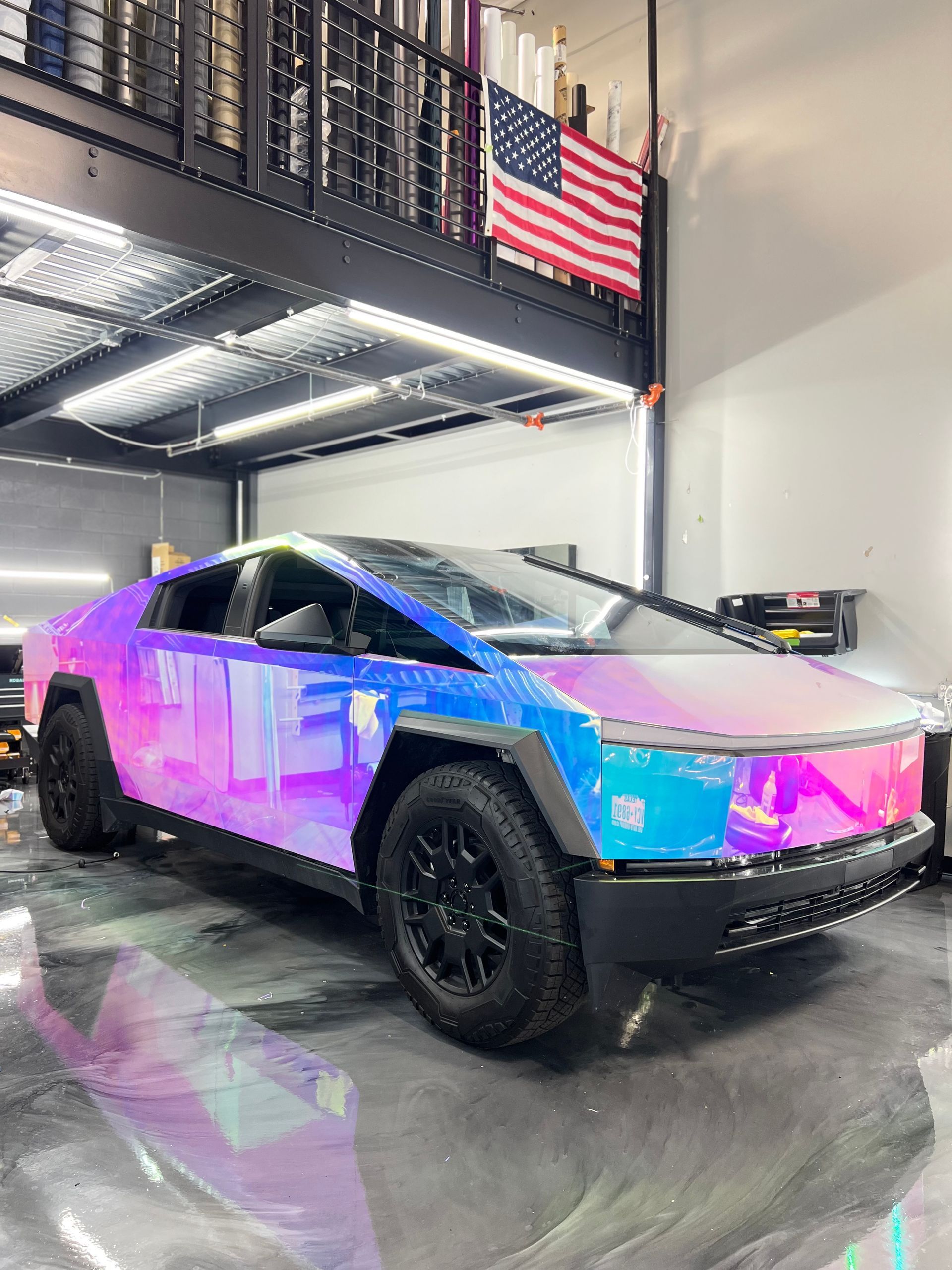 A purple and blue tesla cybertruck is parked in a garage.
