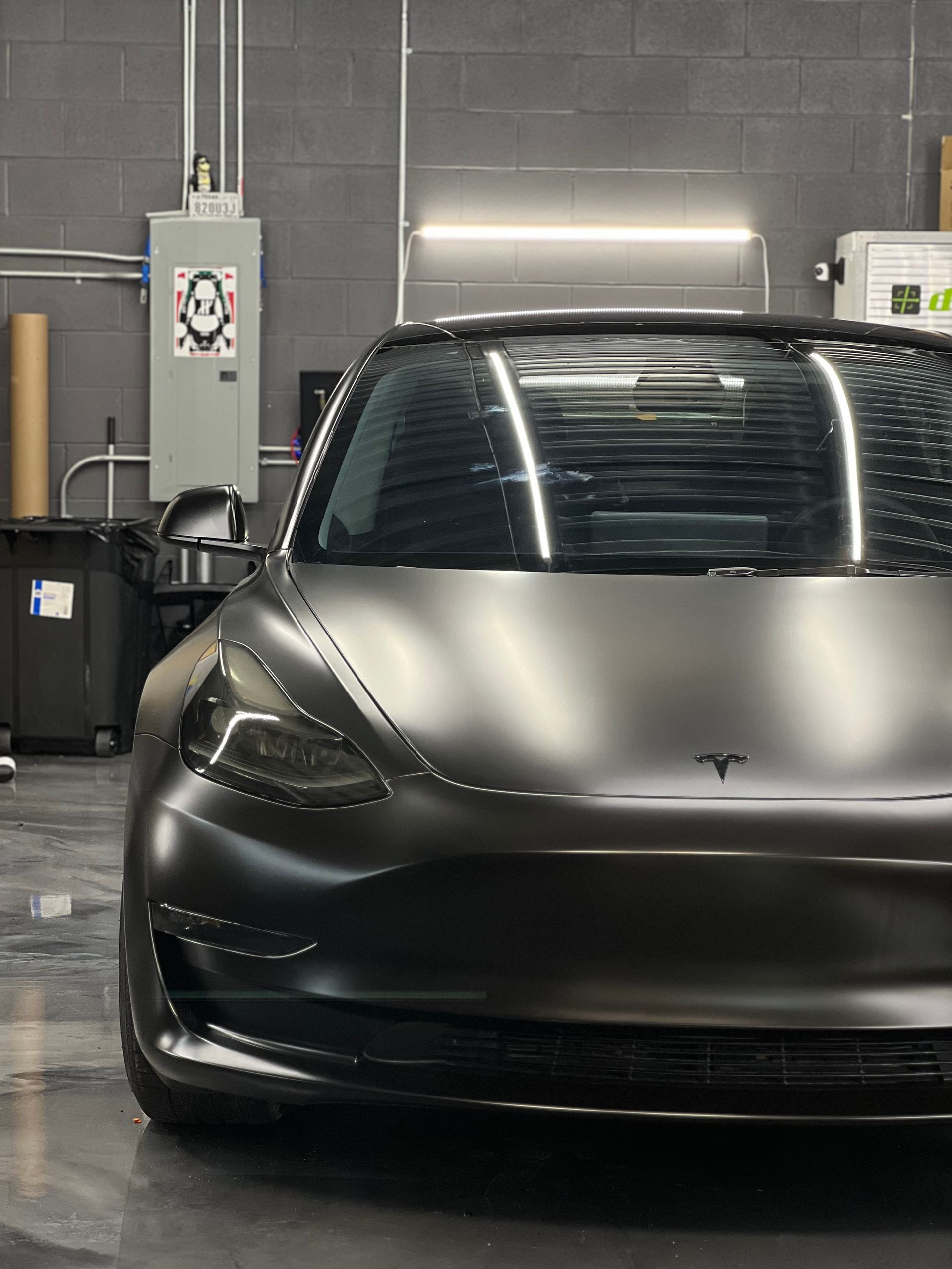 A black tesla model 3 is parked in a garage.