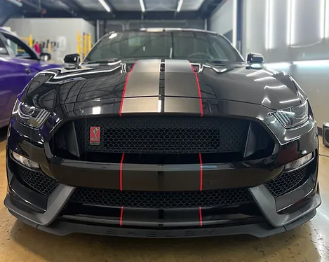 A black ford mustang with red stripes is parked in a garage.