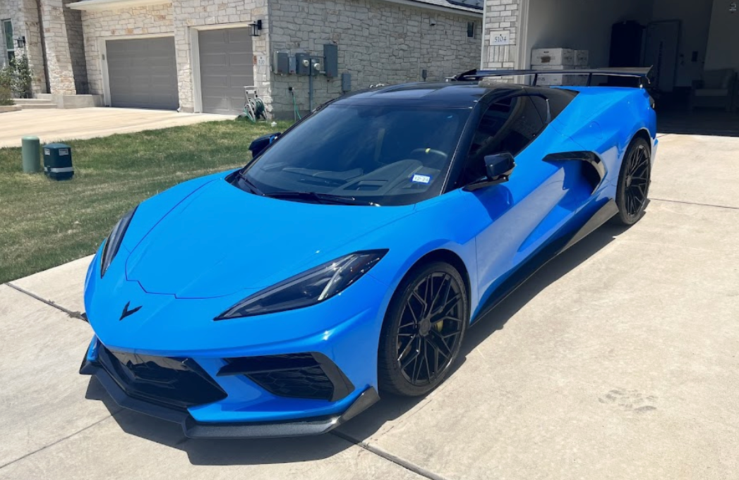 A blue sports car is parked in a driveway in front of a house.