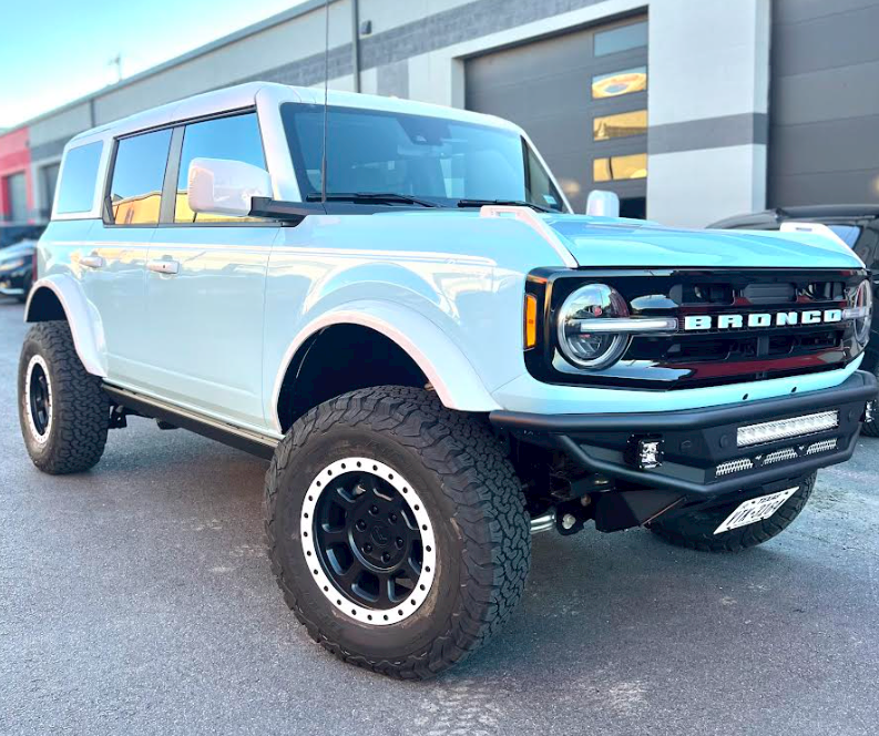 A white ford bronco is parked in front of a building.