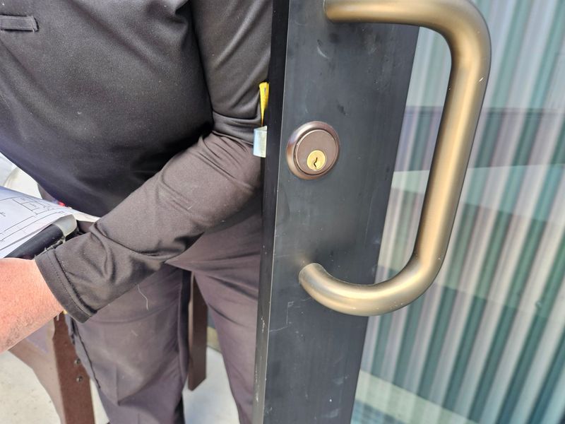 Person in black jacket opening a dark glass door with a brass handle and lock.