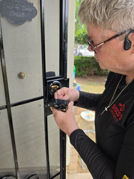 Person unlocking a black mesh security door with a key outside a house.