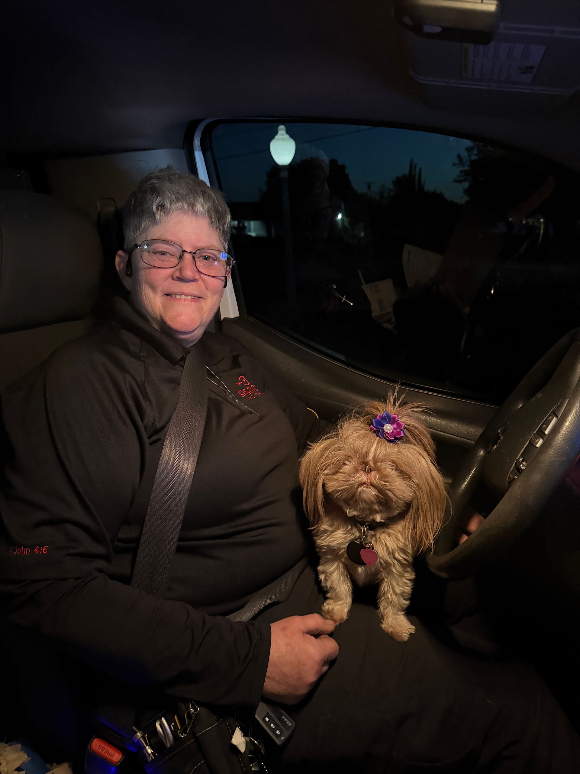 Person sitting in a car at night with a small curly-haired dog on their lap