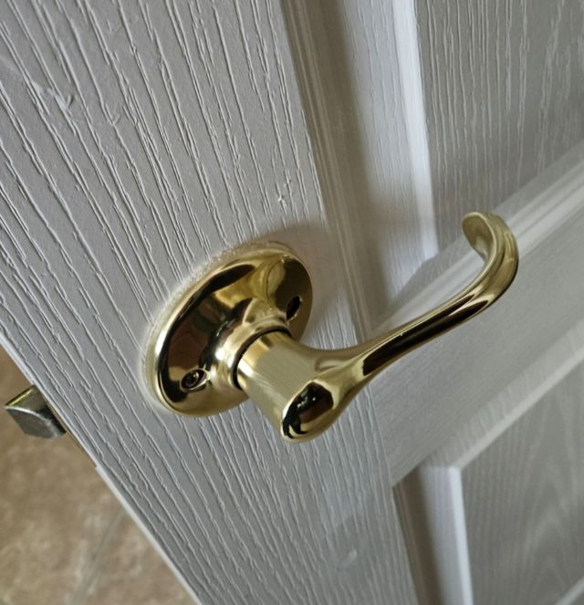 A person in a patterned shirt works on the frame of a wooden door using a metal tool.