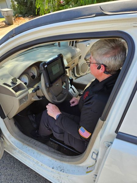 A person sitting in the driver's seat of a car, using a mounted tablet device on the steering wheel.