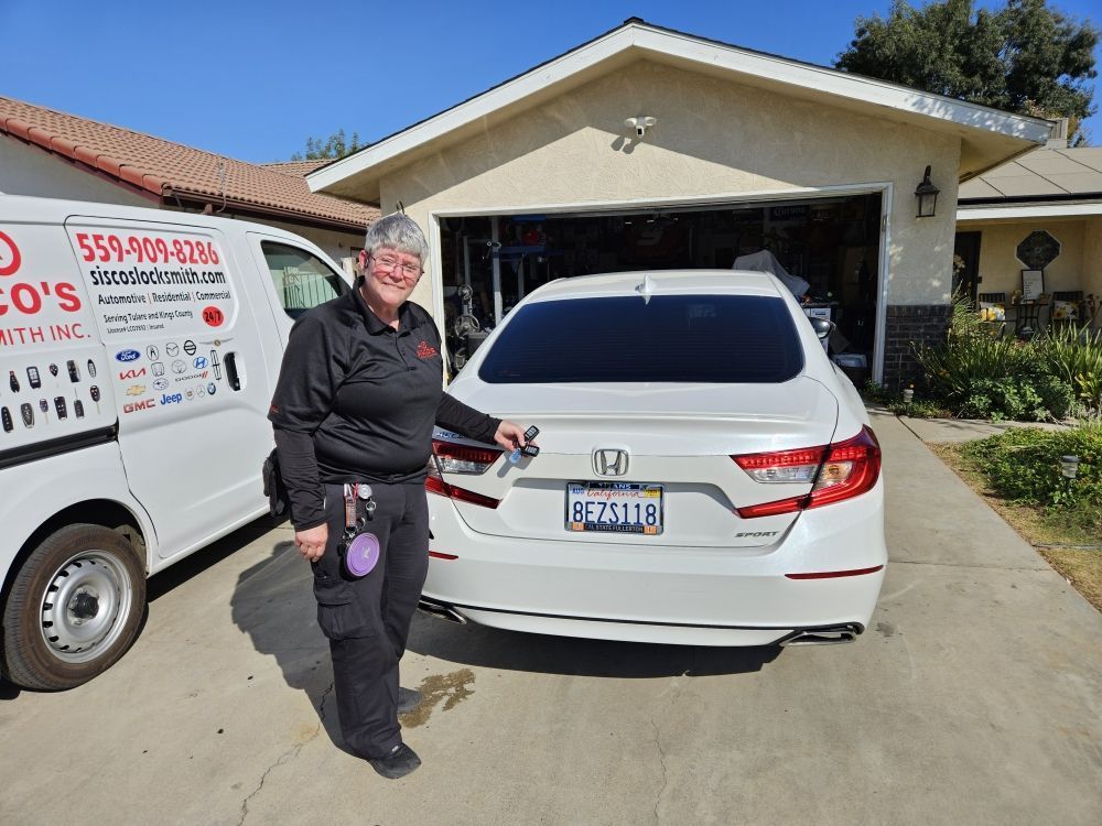 A locksmith standing by a white Honda in a driveway next to their work van.