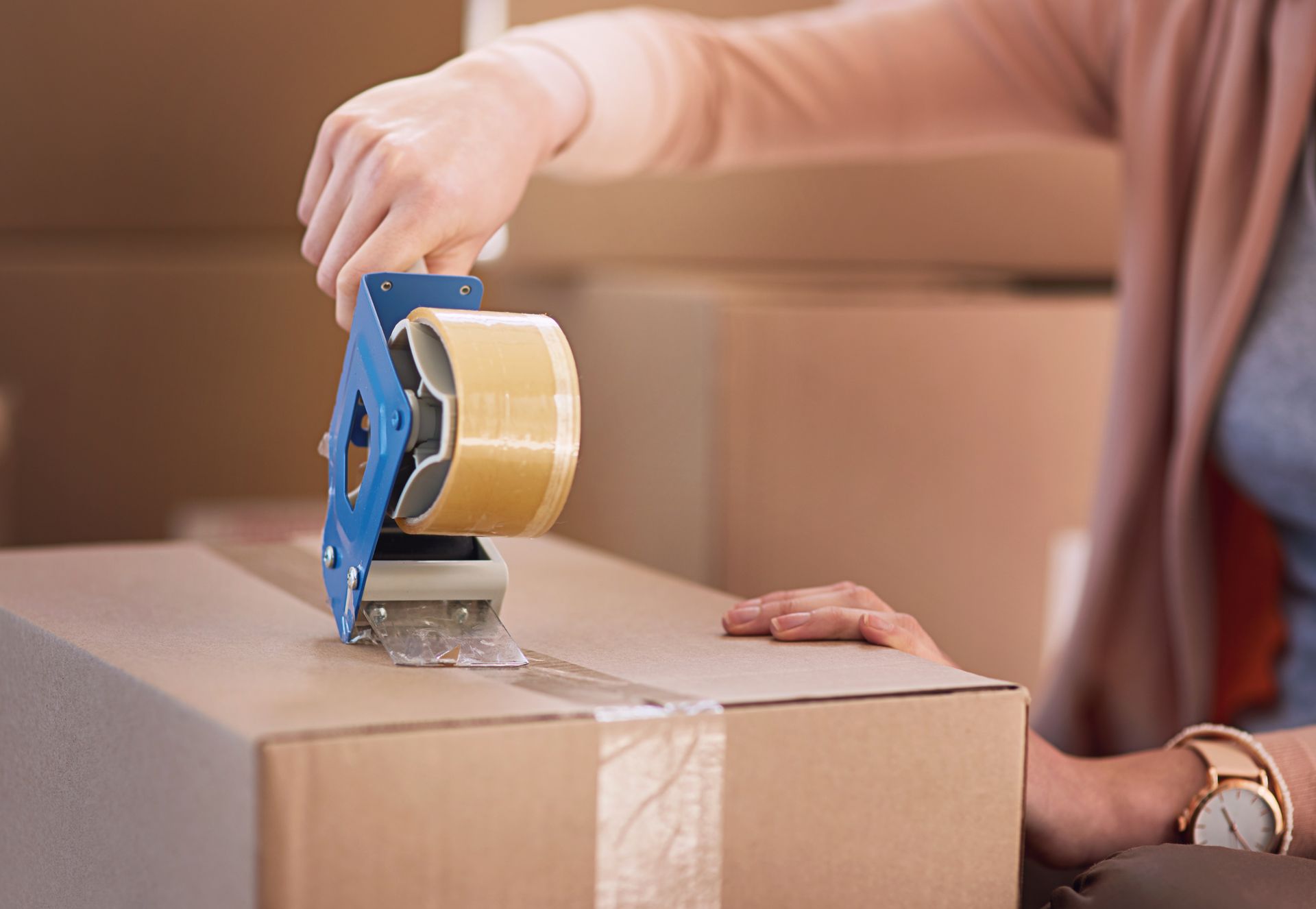 Person sealing a cardboard box with tape dispenser.