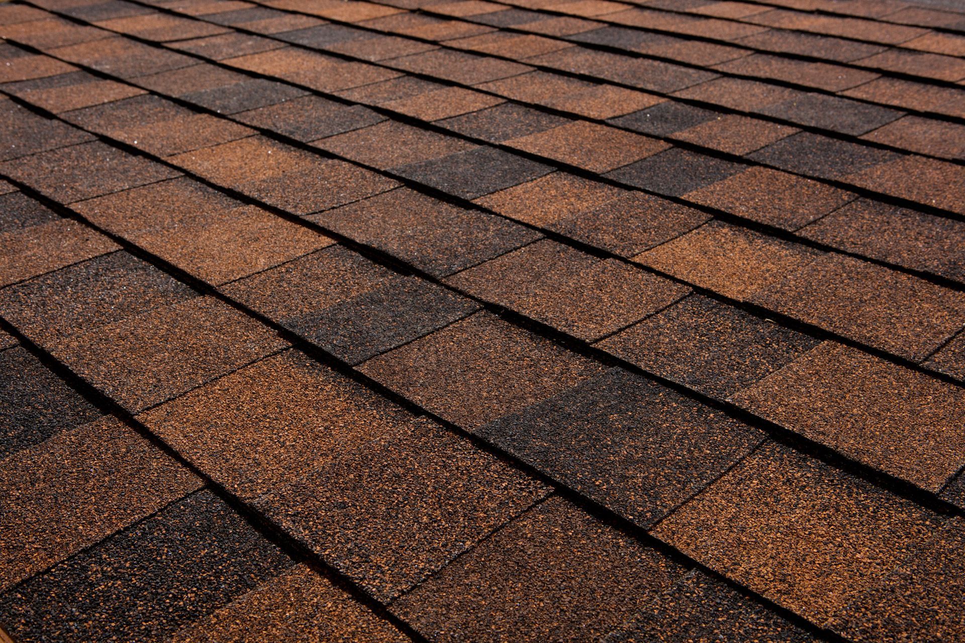 Close-up of brown and black asphalt roof shingles in a repeating pattern.