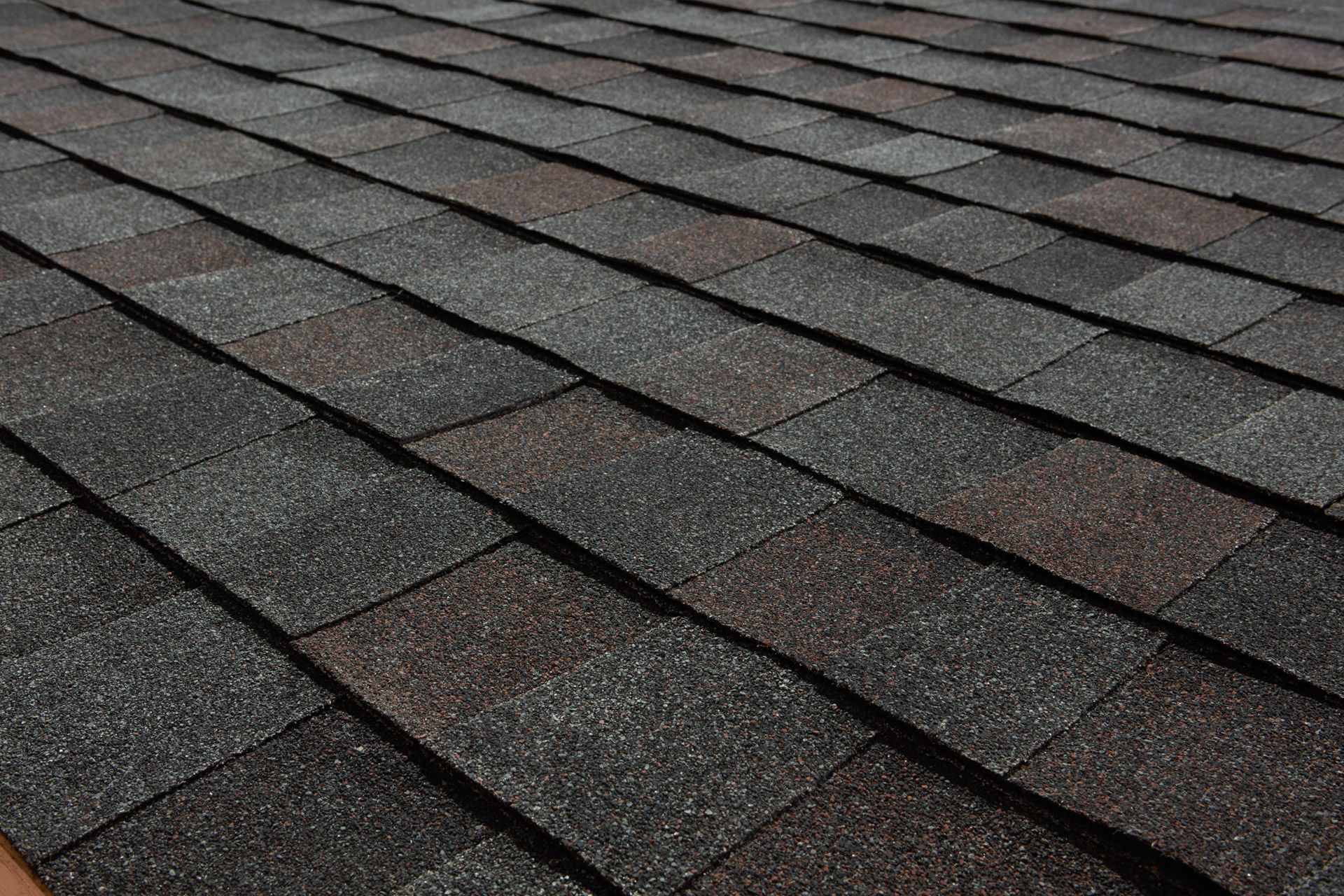 Dark asphalt shingles with brown and gray tones, covering a roof.