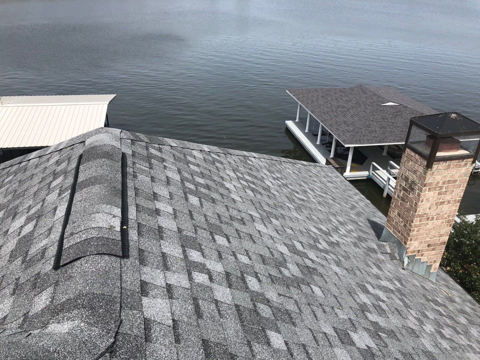 Gray asphalt shingle roof, brick chimney, overlooking a lake with docks.