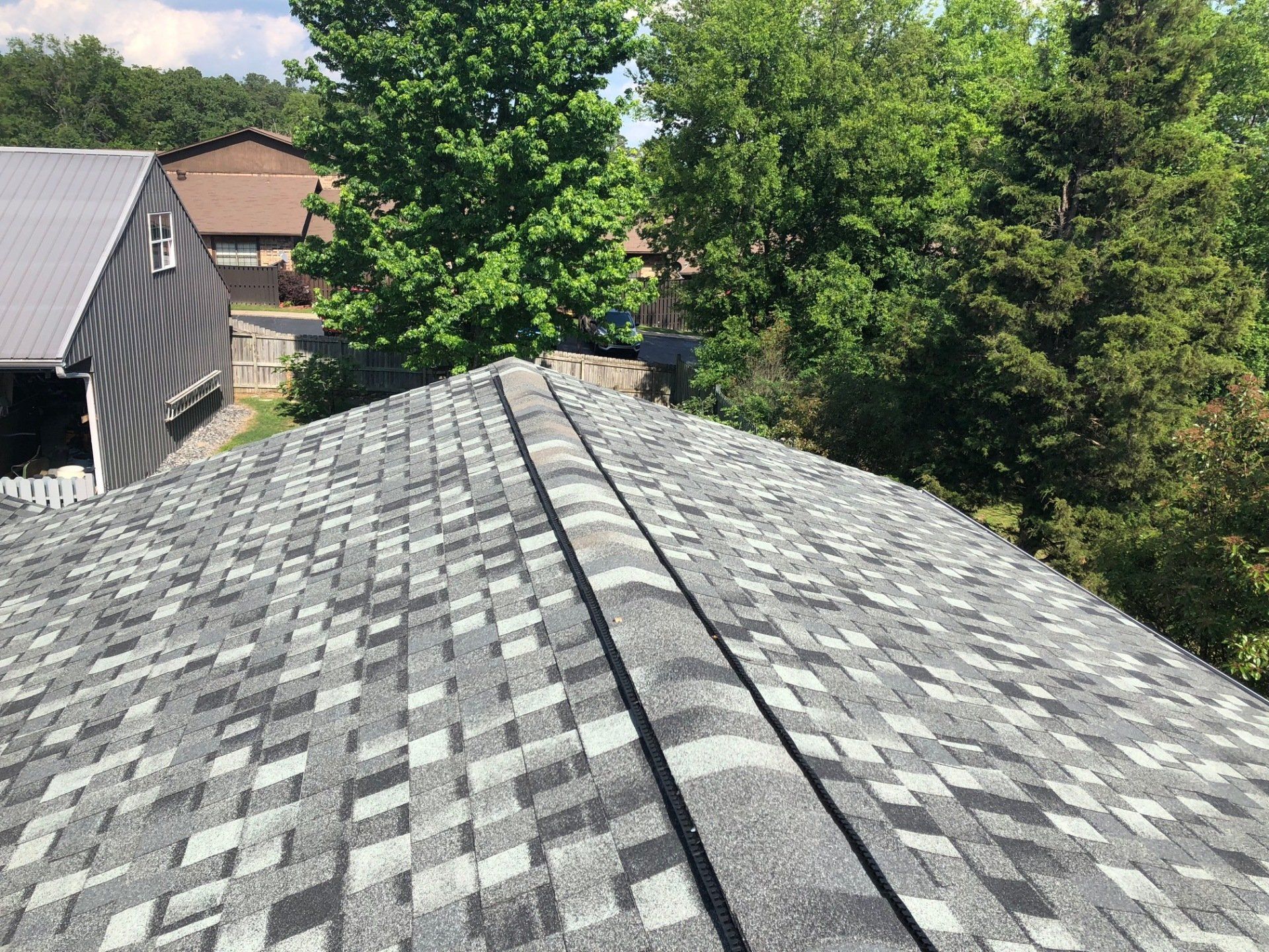 Gray asphalt shingle roof with a central ridge, trees and a building in the background.