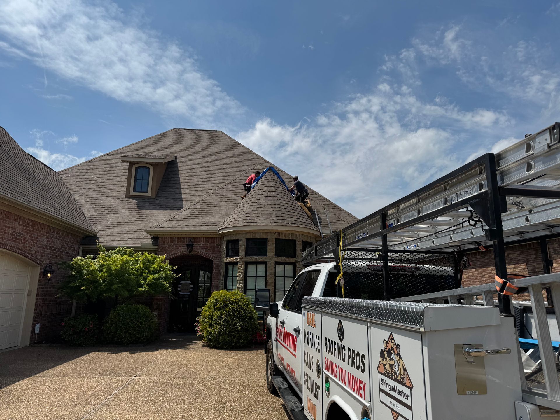 Roofers on a house roof next to a work truck on a sunny day.
