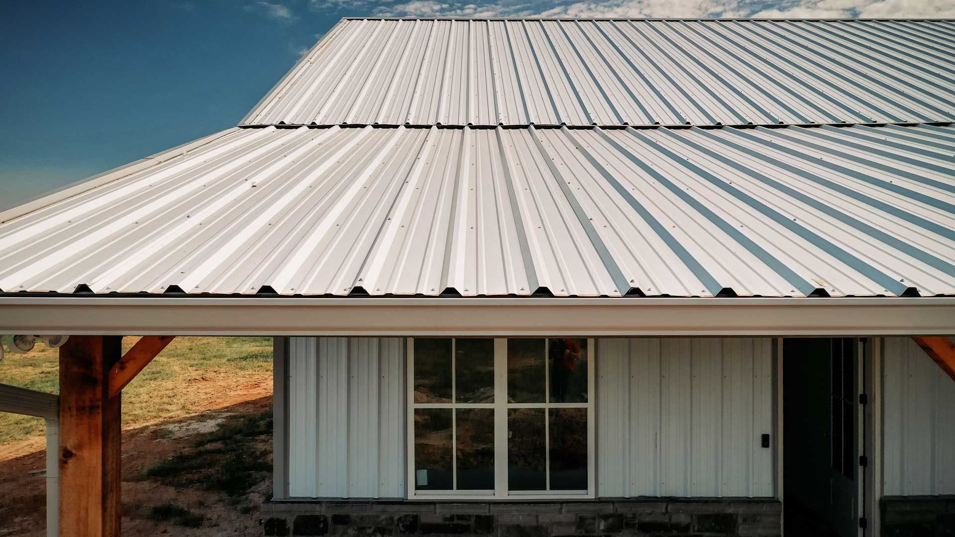 White metal roof on a white building with a window and a door, bright sky.
