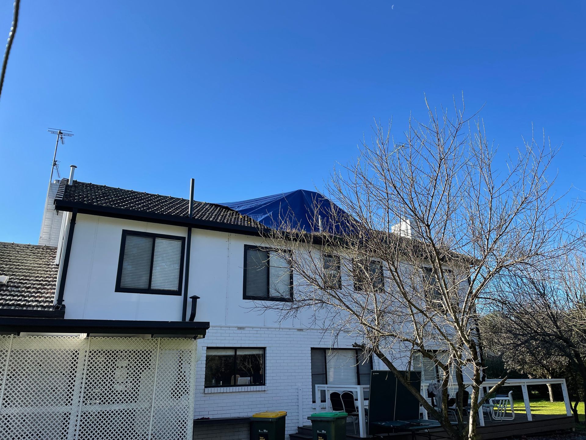 A white house with a blue tarp on the roof — Stephen Meaker Roofing in Wagga Wagga, NSW