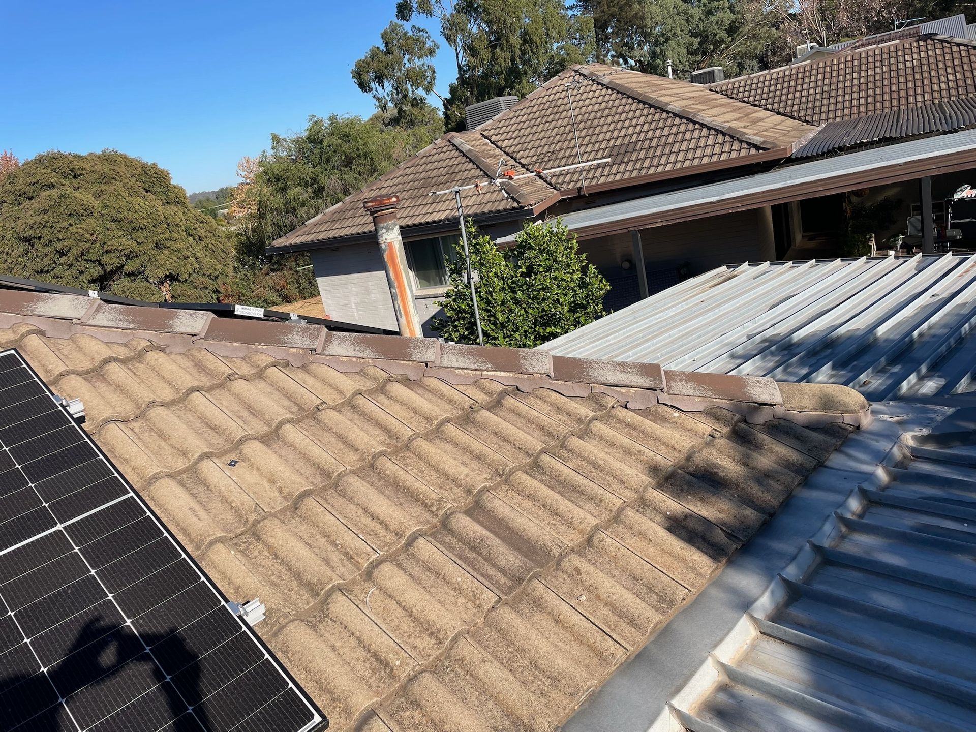 A roof with solar panels on it and a house in the background — Stephen Meaker Roofing in Wagga Wagga, NSW