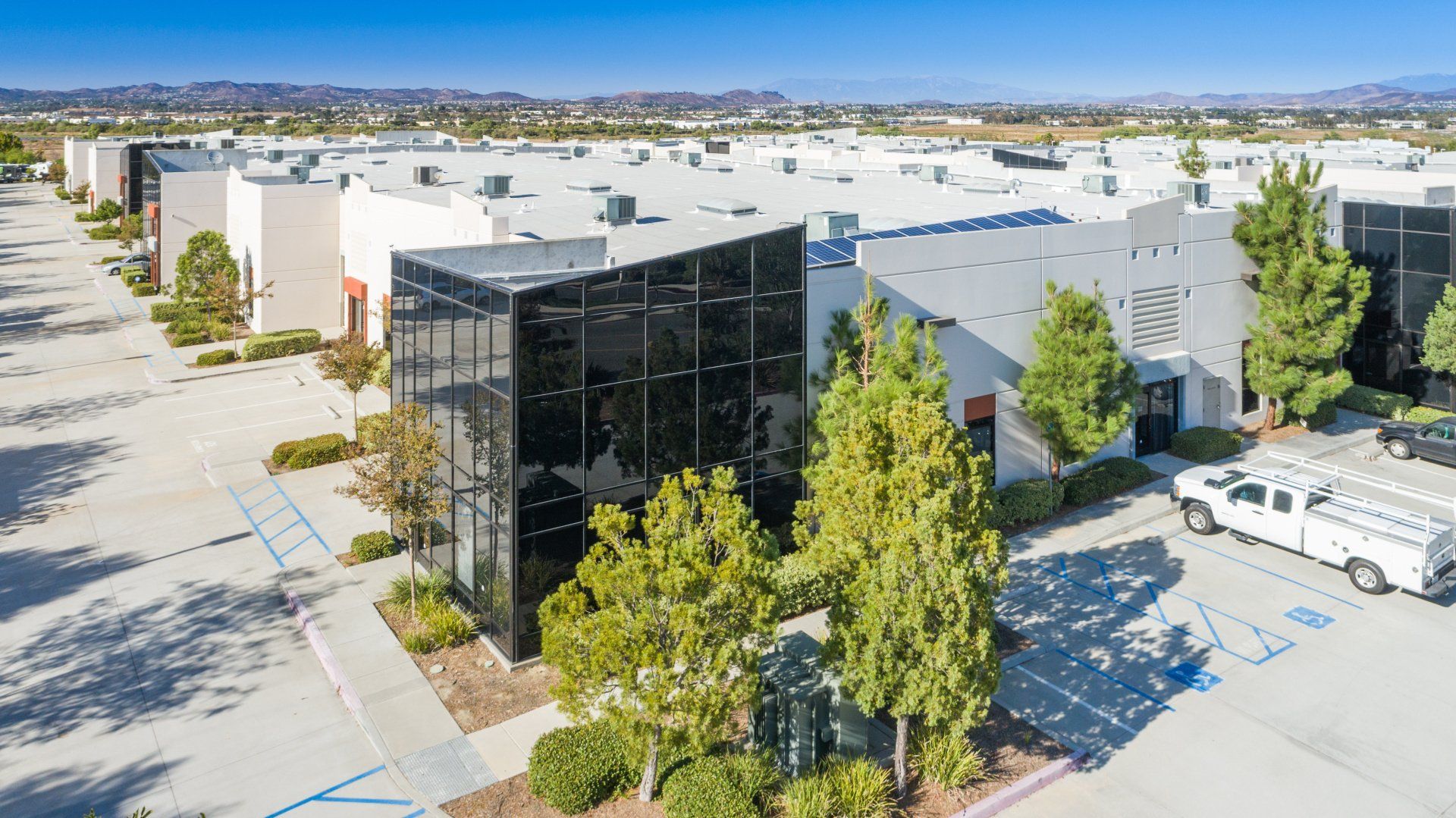 Aerial view of a business complex with buildings, parking, and trees under a blue sky.