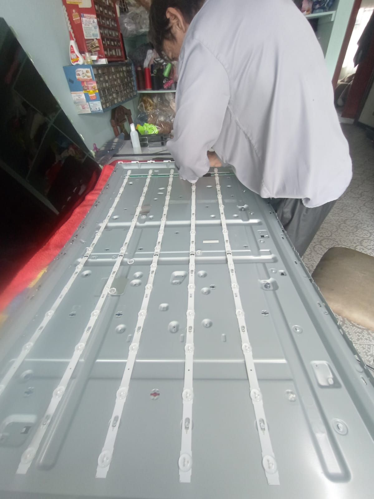 Persona trabajando en la parte posterior abierta de un televisor con tiras de luz LED visibles.