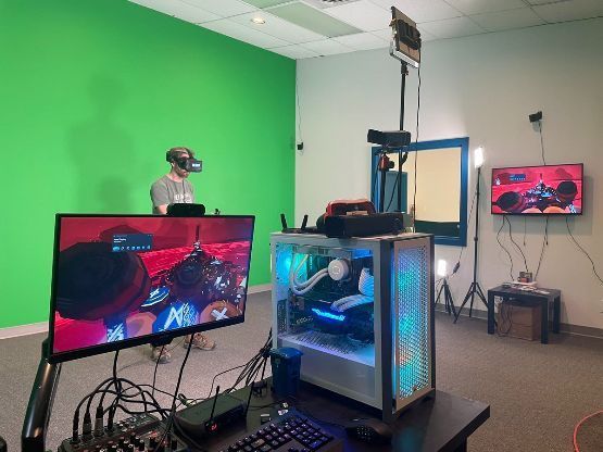 A man wearing a virtual reality headset is playing a video game in front of a green screen.