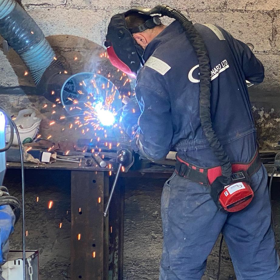 A man wearing a welding helmet is welding a piece of metal