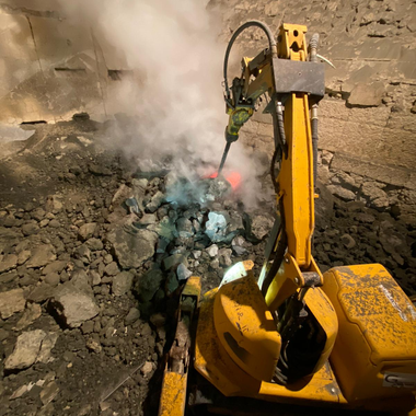 A yellow excavator is breaking rocks with a hammer