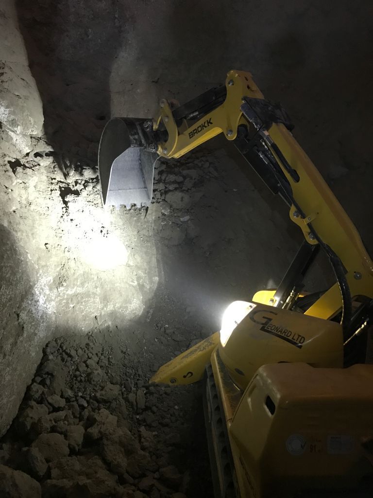 A yellow excavator is digging a hole in the ground at night.