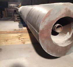 A large metal pipe with a hole in the middle is sitting on a wooden floor.