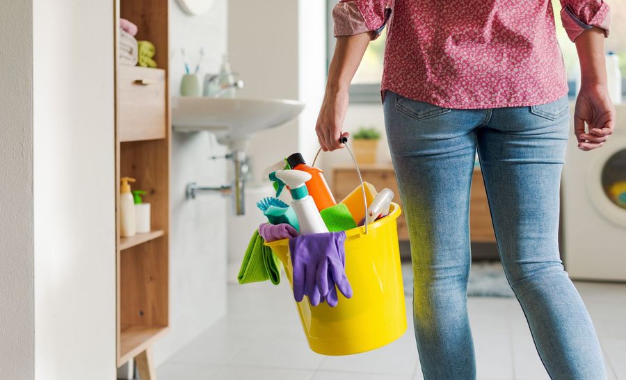 A person carrying a bright yellow bucket filled with cleaning supplies in a home environment.
