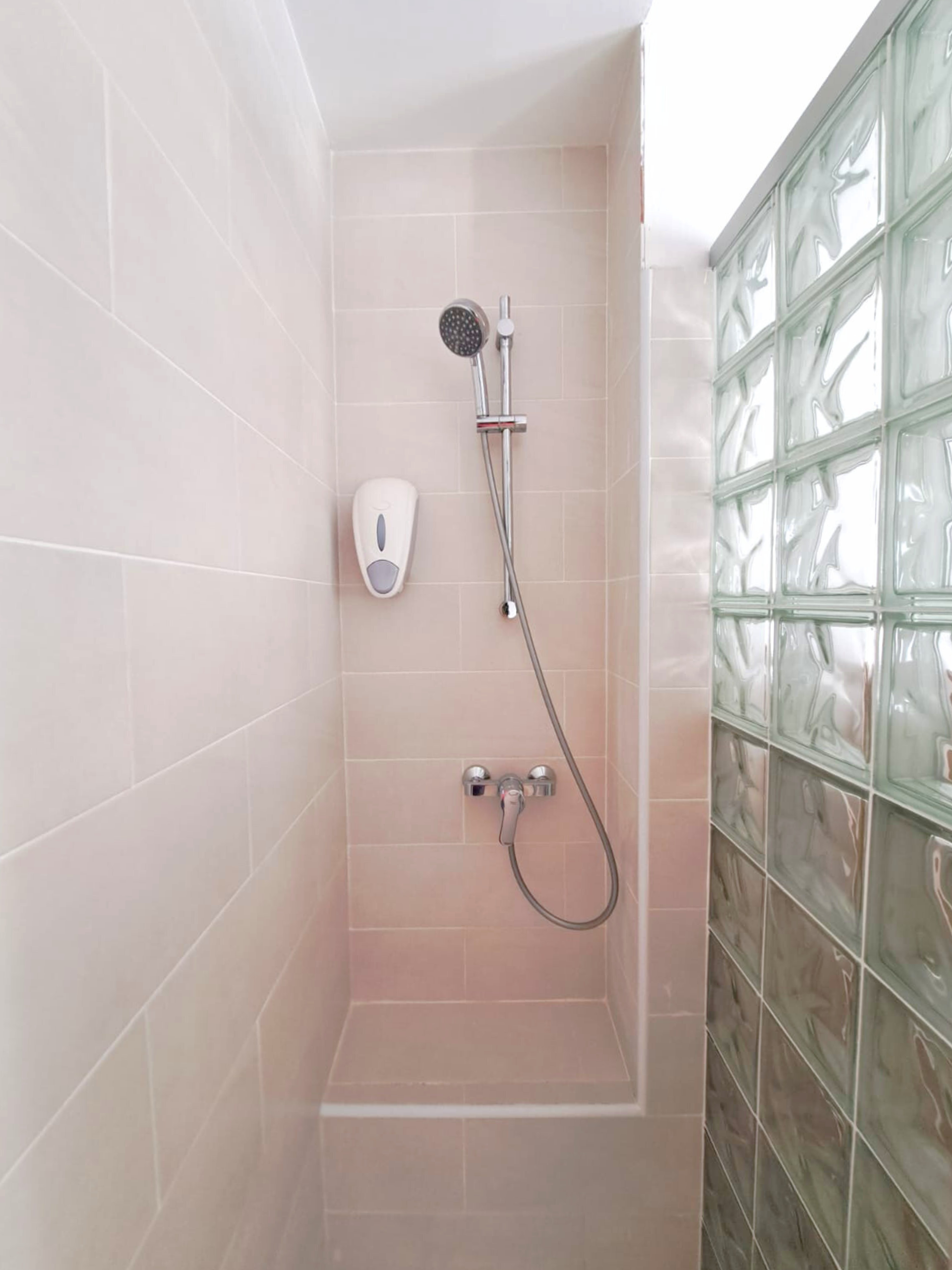A beige tiled shower stall featuring a handheld showerhead, chrome faucet, and a wall-mounted soap dispenser.