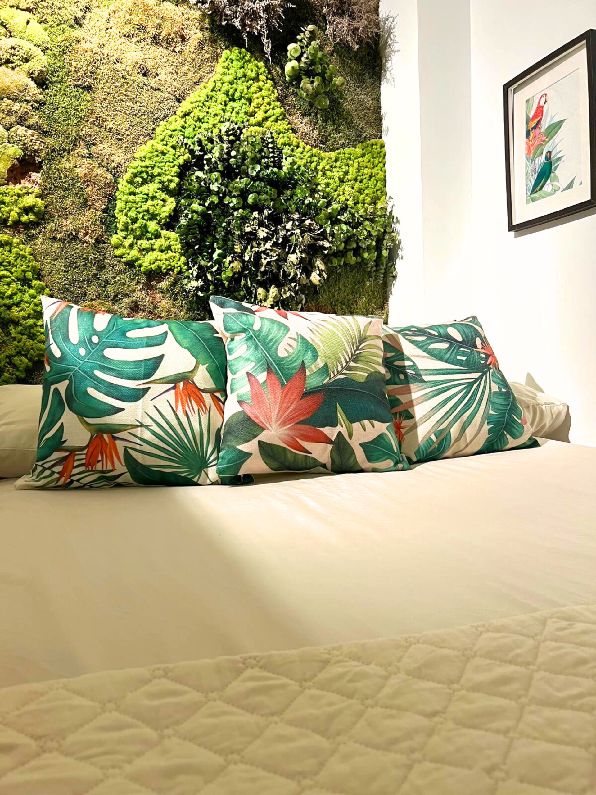 A bed with tropical-patterned throw pillows in front of a lush, indoor vertical garden wall and framed artwork.