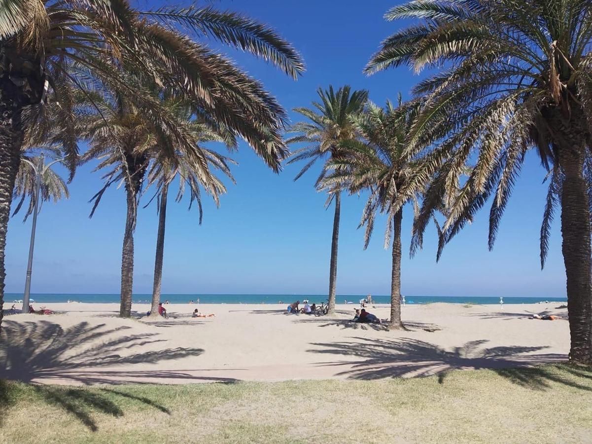 A sunny beach scene framed by palm trees with people relaxing on the sand near the ocean.