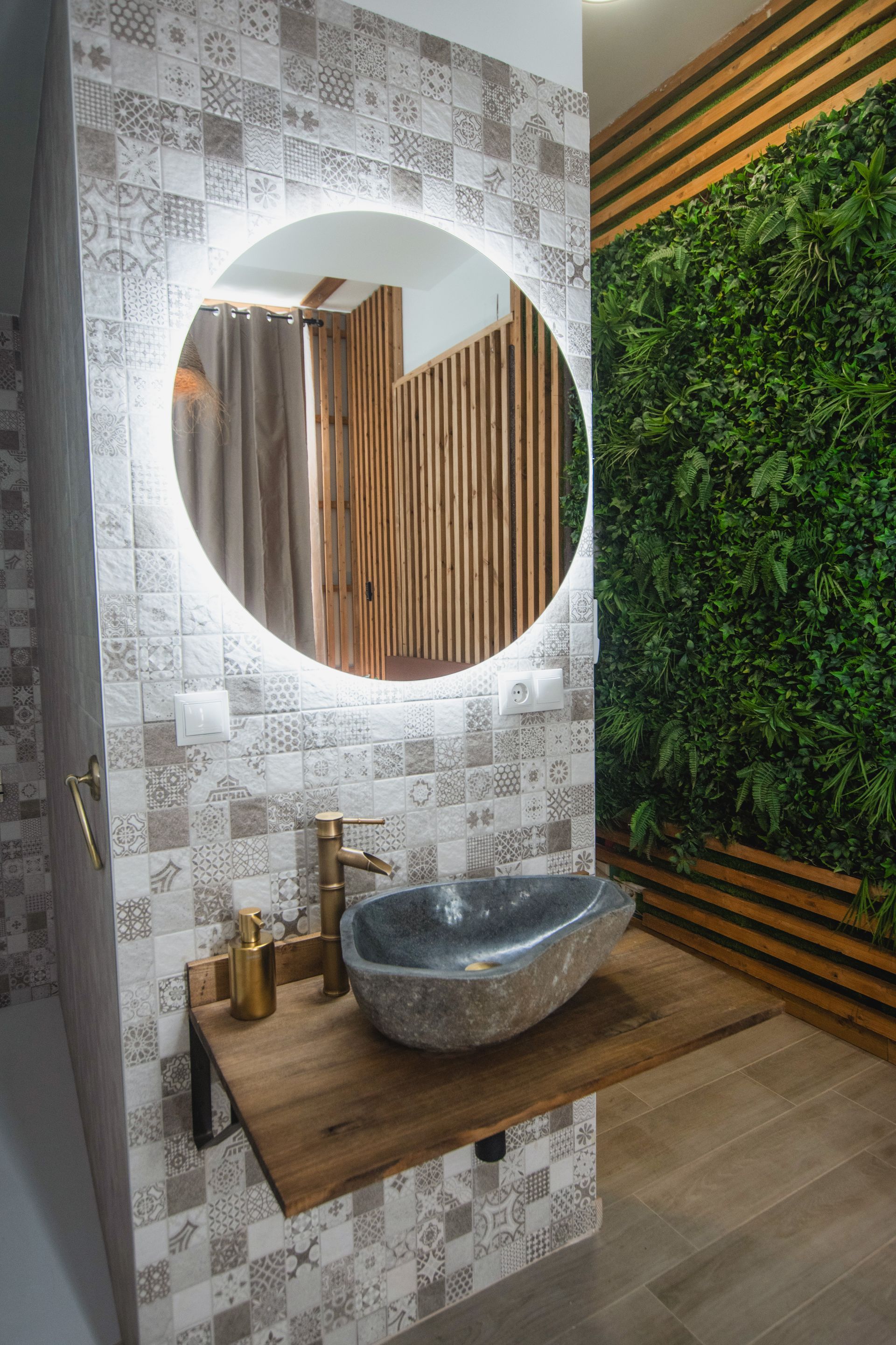 Modern bathroom vanity featuring a stone vessel sink on a wooden shelf, a backlit round mirror, and a green wall feature.