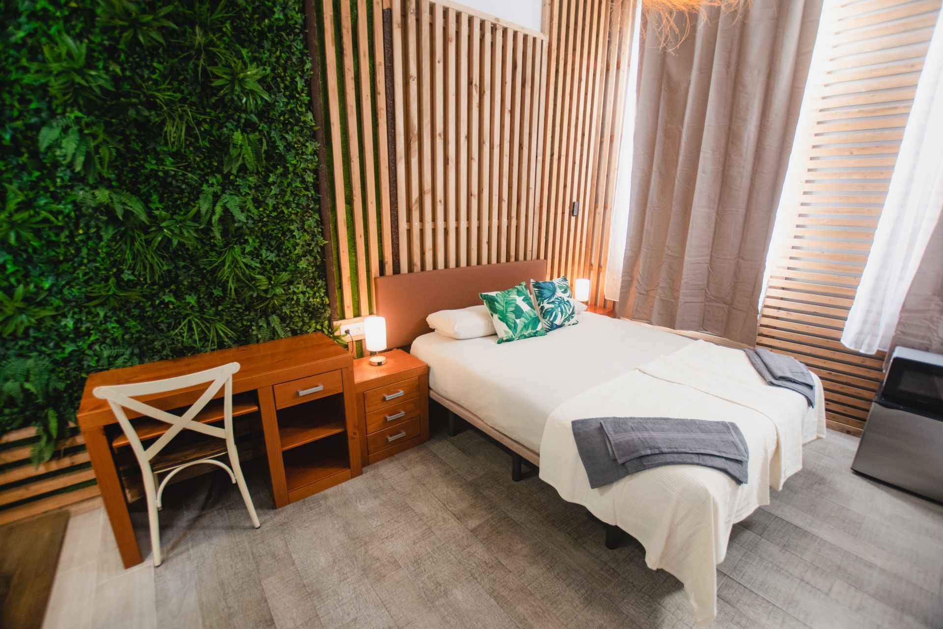 A modern bedroom with a bed, wooden desk and chair, and a vertical garden wall feature.