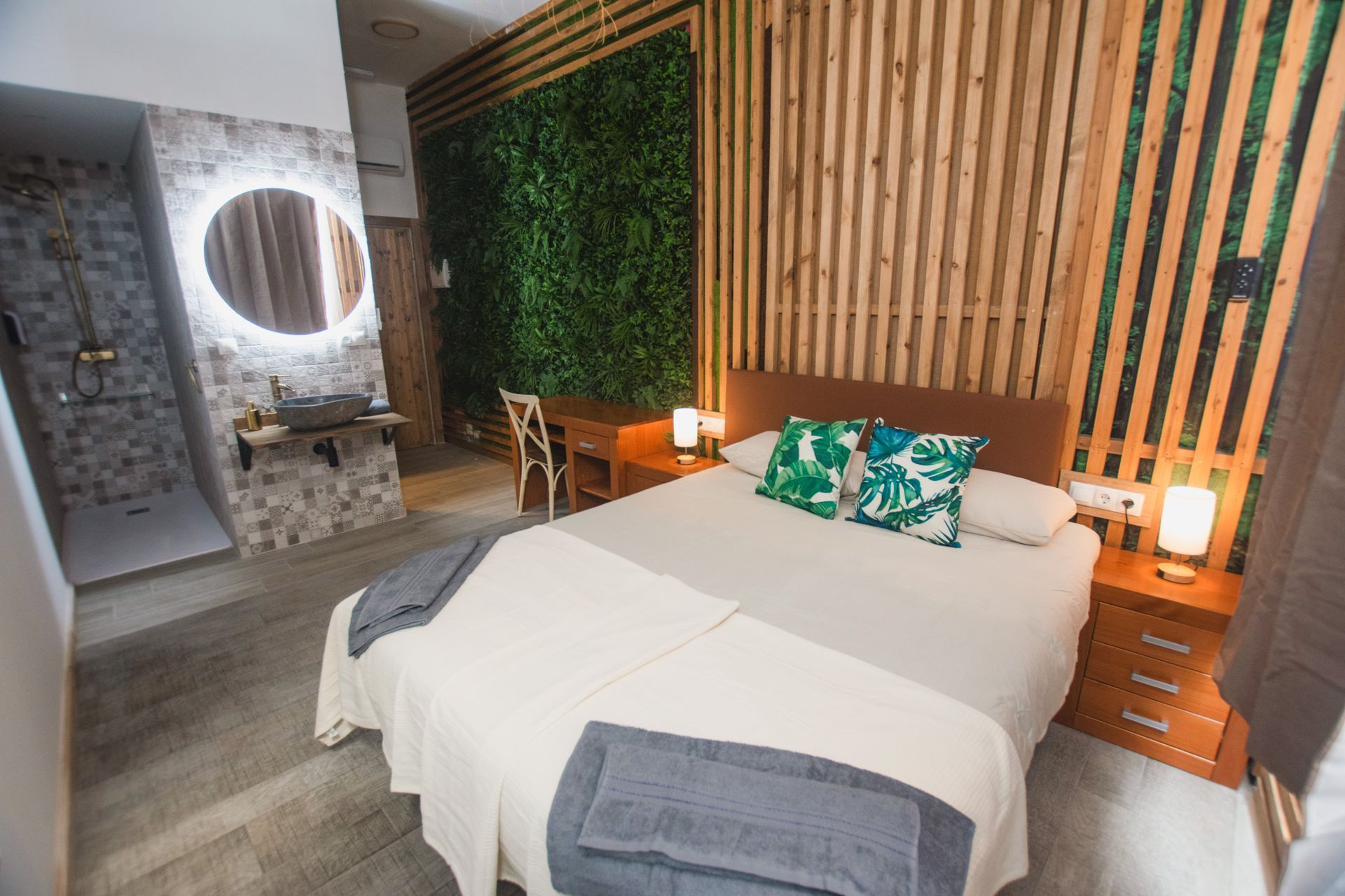 Modern hotel room with a queen bed, green wall feature, wooden slat accents, open-concept vanity, and walk-in shower.
