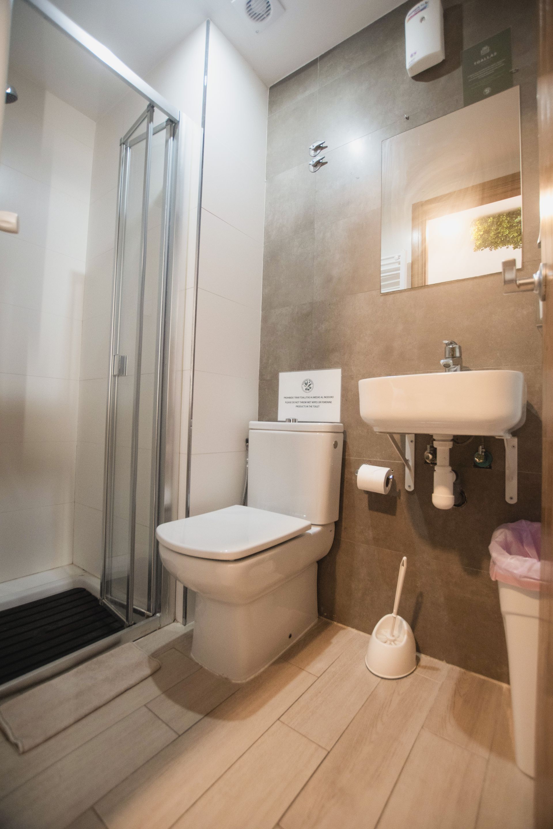 A modern, compact bathroom with a shower stall, white toilet, wall-mounted sink, and beige tile floor.