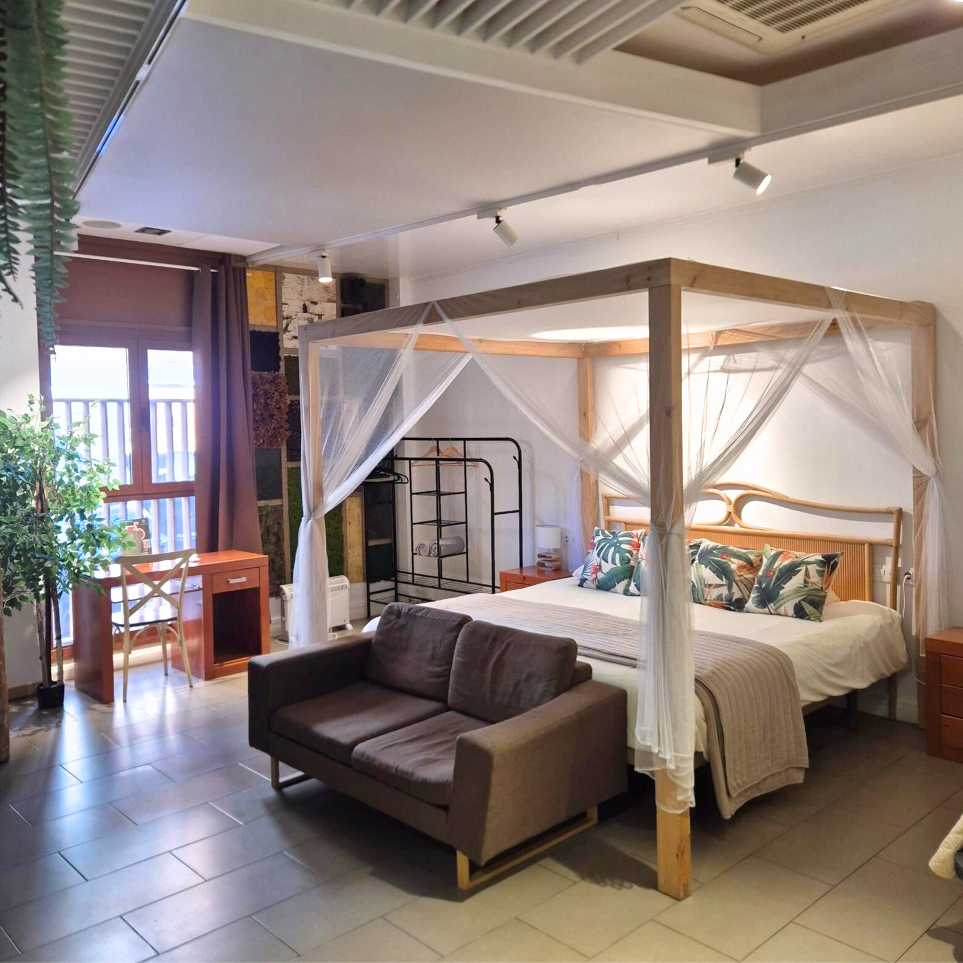 A canopy bed with white curtains, a brown sofa, and a desk in a room with tiled floors and wooden accents.