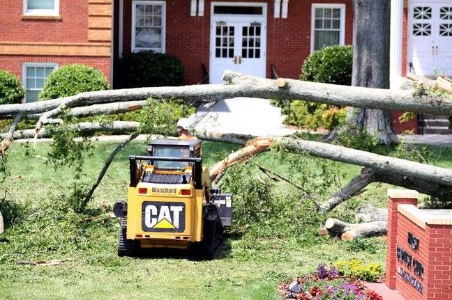 Yellow CAT skid steer clearing fallen tree branches in front of a brick building.