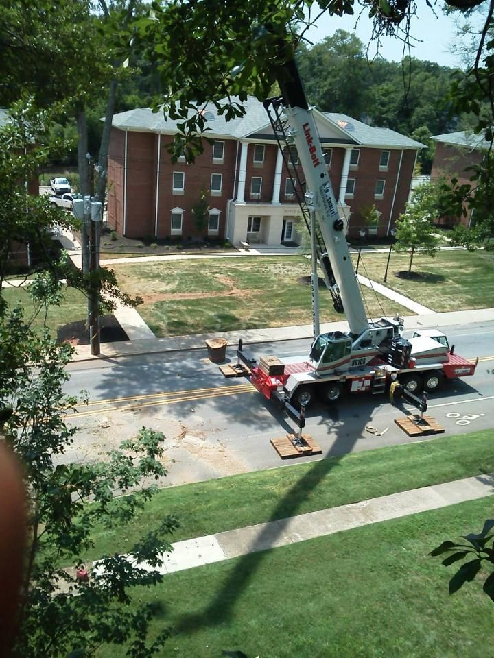 Crane on a truck in front of a brick building, possibly a dormitory. Trees and grass surround the area.