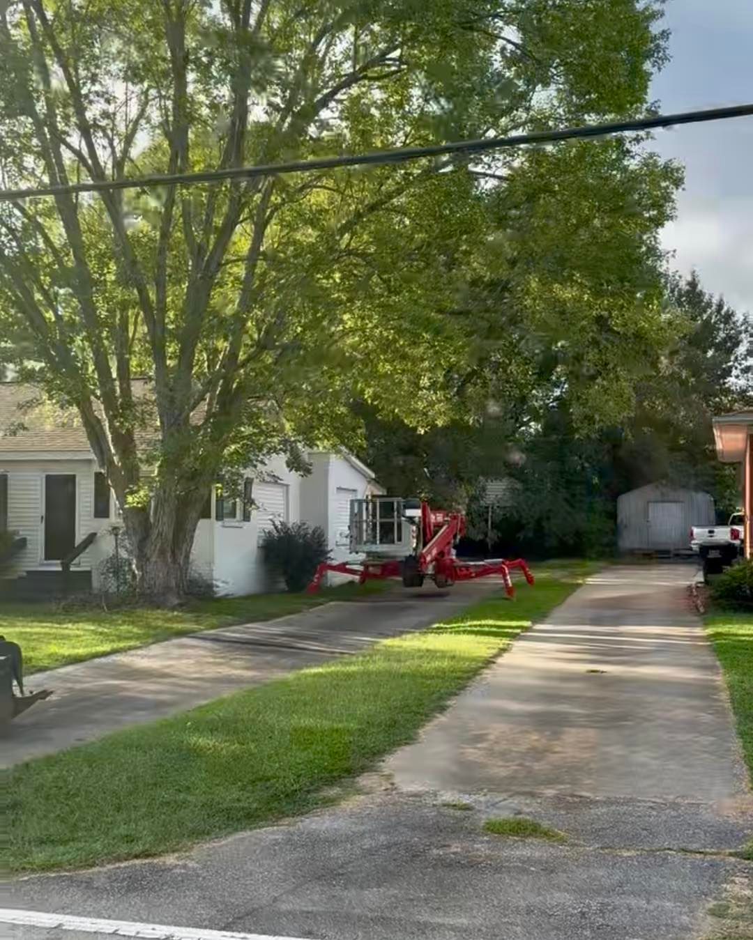 A white house with a tree in front. A red lift sits in the driveway.