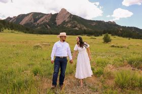 A man and a woman are holding hands in a field with mountains in the background.