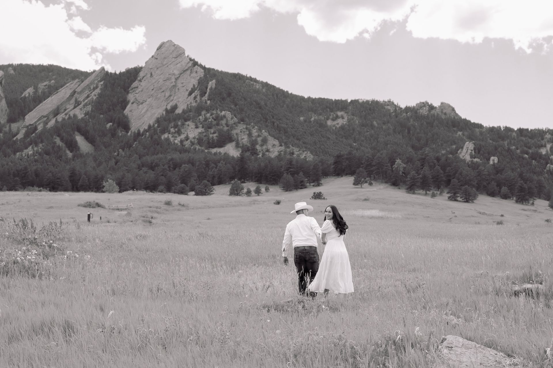 A man and a woman are walking through a field with mountains in the background.