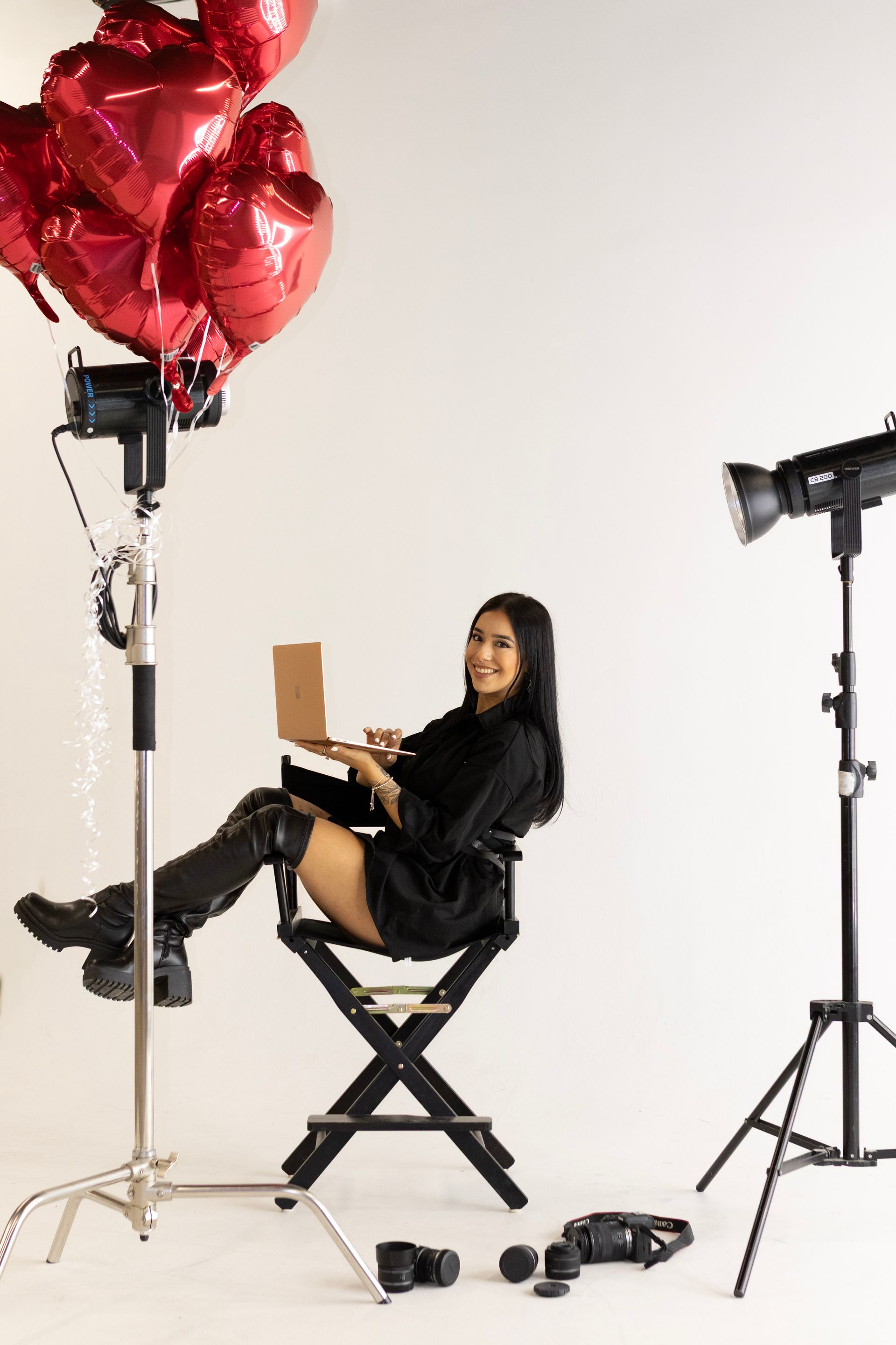 A woman is sitting in a director 's chair with a laptop and balloons.