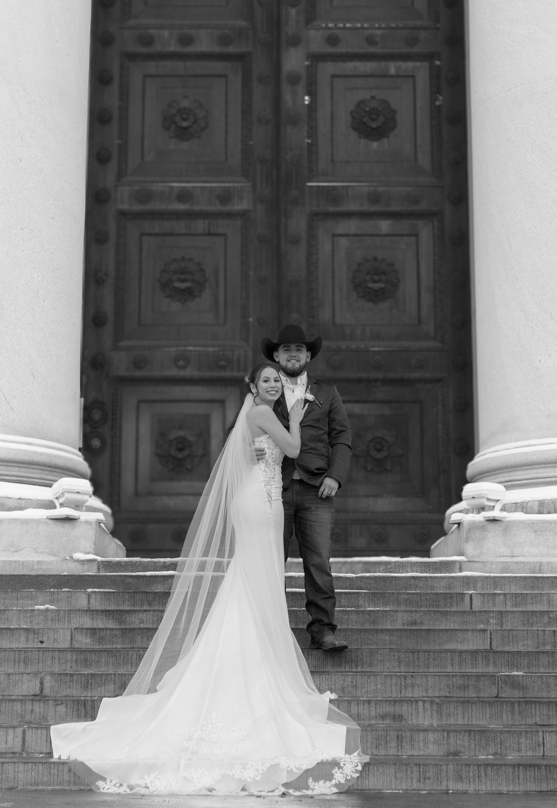 A bride and groom are posing for a black and white photo on the steps of a building.