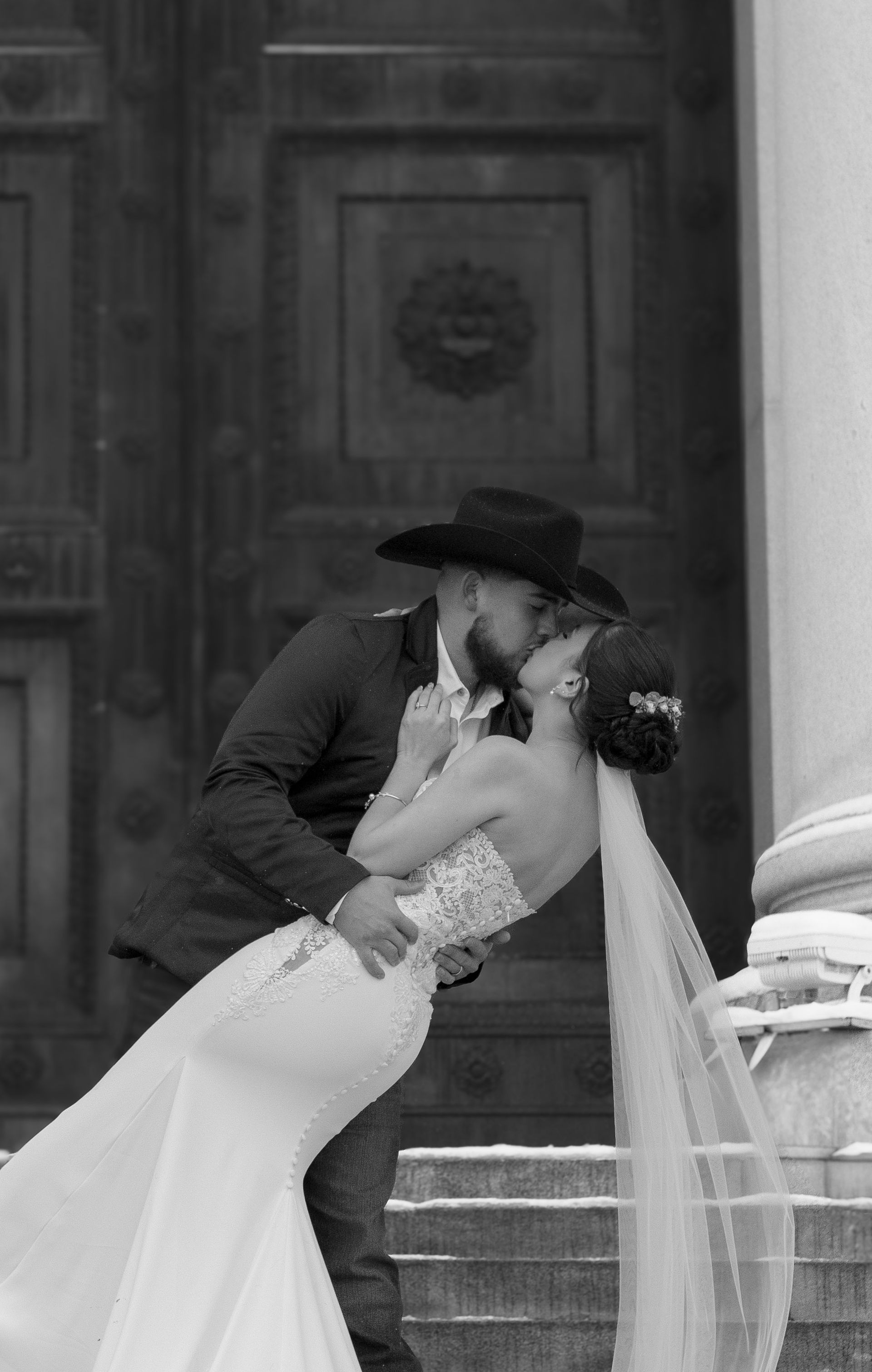 A bride and groom are kissing in front of a building.