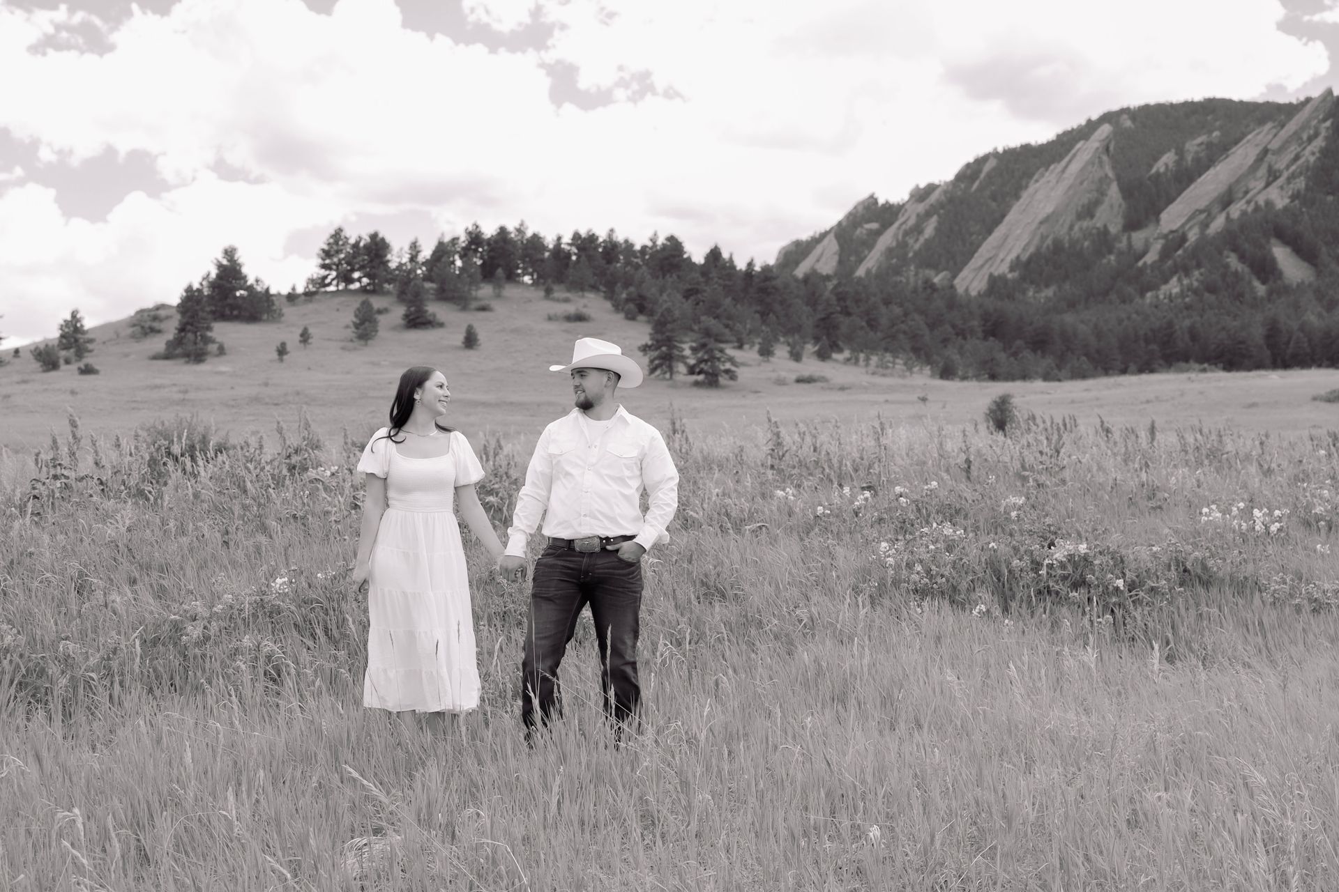A man and a woman are standing in a field holding hands.